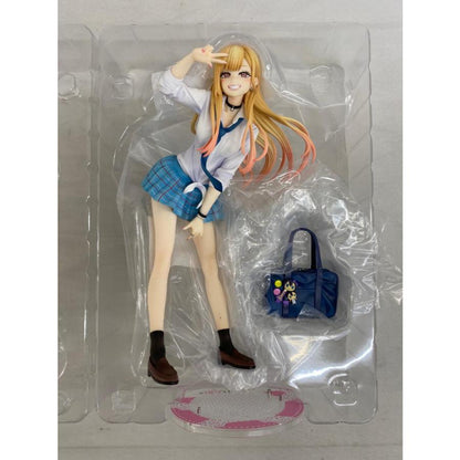A blonde anime figure in a plastic blister tray with a small handbag accessory and a display base.