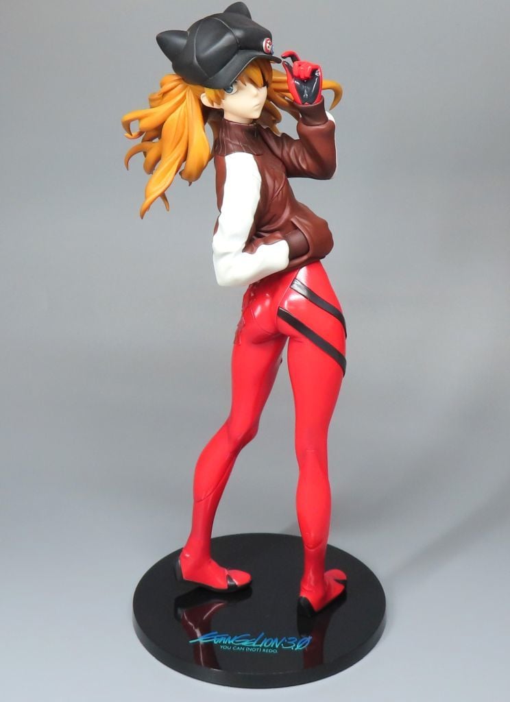 Asuka Langley figure in a brown jacket, red leggings, and black cat-eared cap on a round black base.