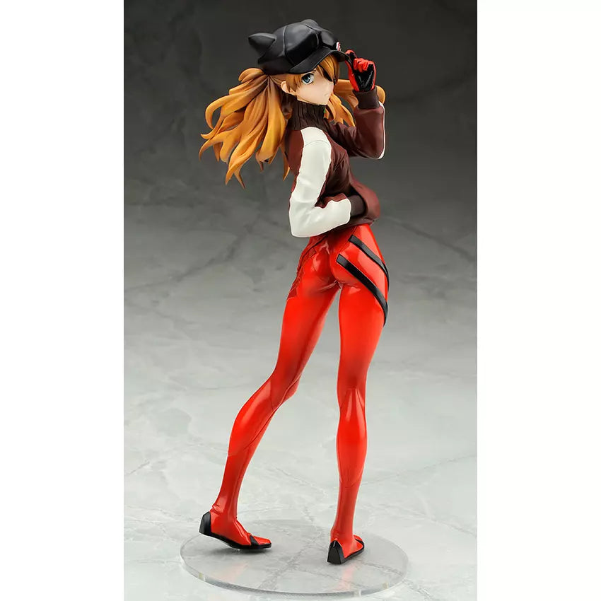A posed anime figure of Asuka in a brown jacket, red pants, and black cap on a clear base.