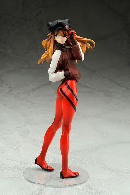 Anime girl figure standing on a clear round base, wearing a black cap, brown jacket, and red leggings.