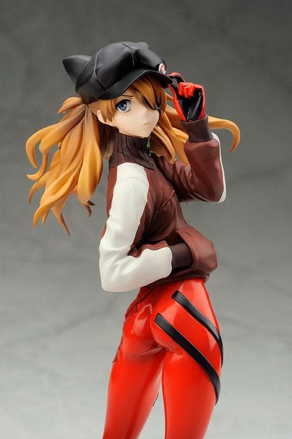 An anime figure of Asuka Langley posing in a cap, jacket, and red pants on a plain gray background.