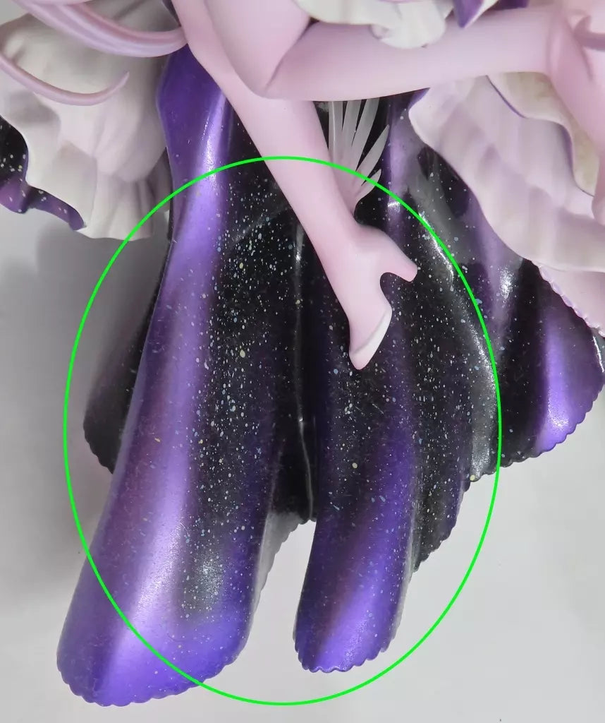 Close-up of a figure’s purple and black dress and pale leg against a white background