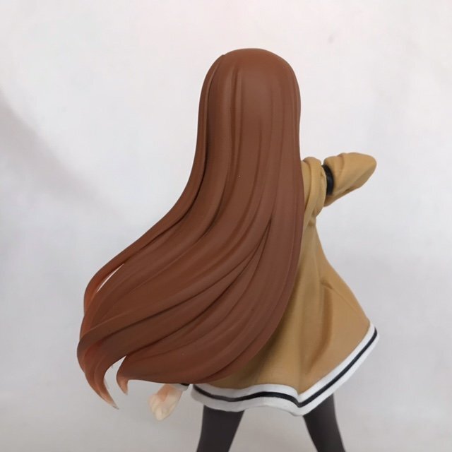Rear view of a long-haired anime figure in a tan coat on a plain light background.