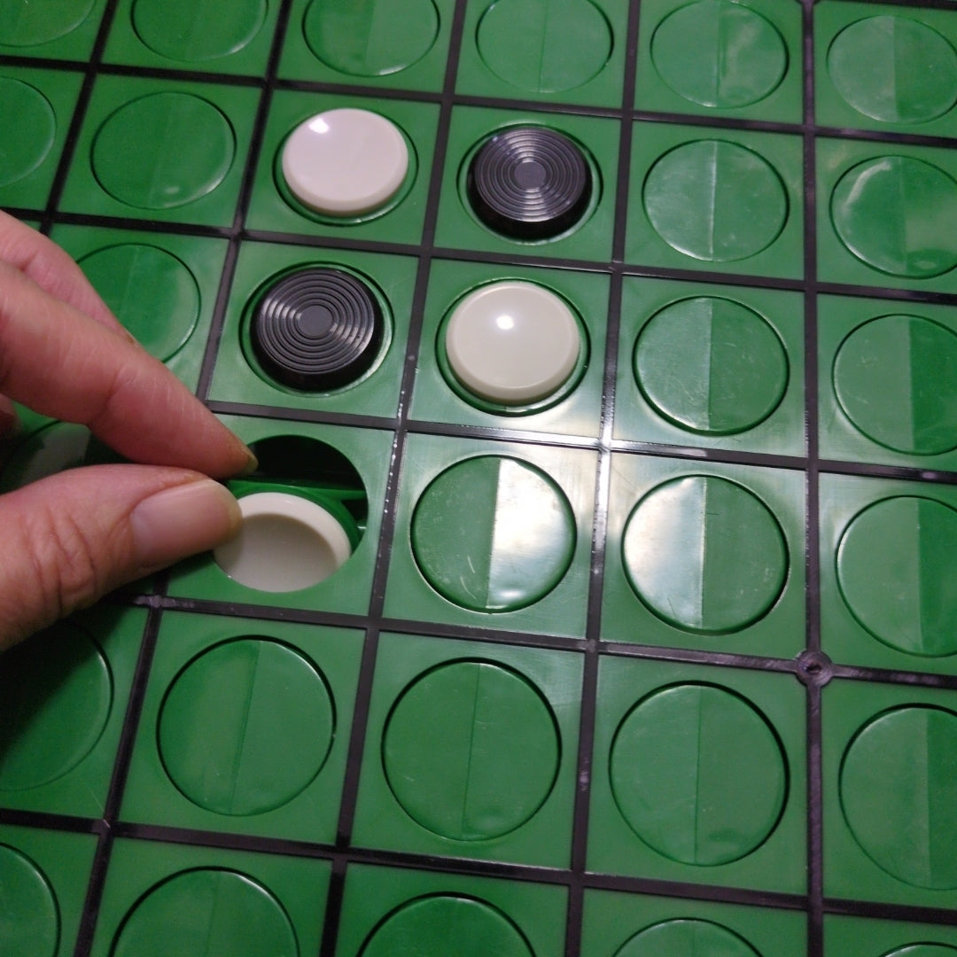 Close-up of an Othello game board with black and white discs and a hand placing one piece.