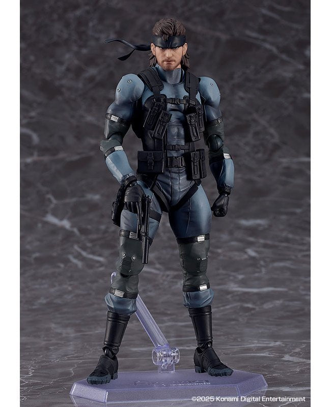 A posed action figure of Solid Snake standing on a clear stand against a dark backdrop.