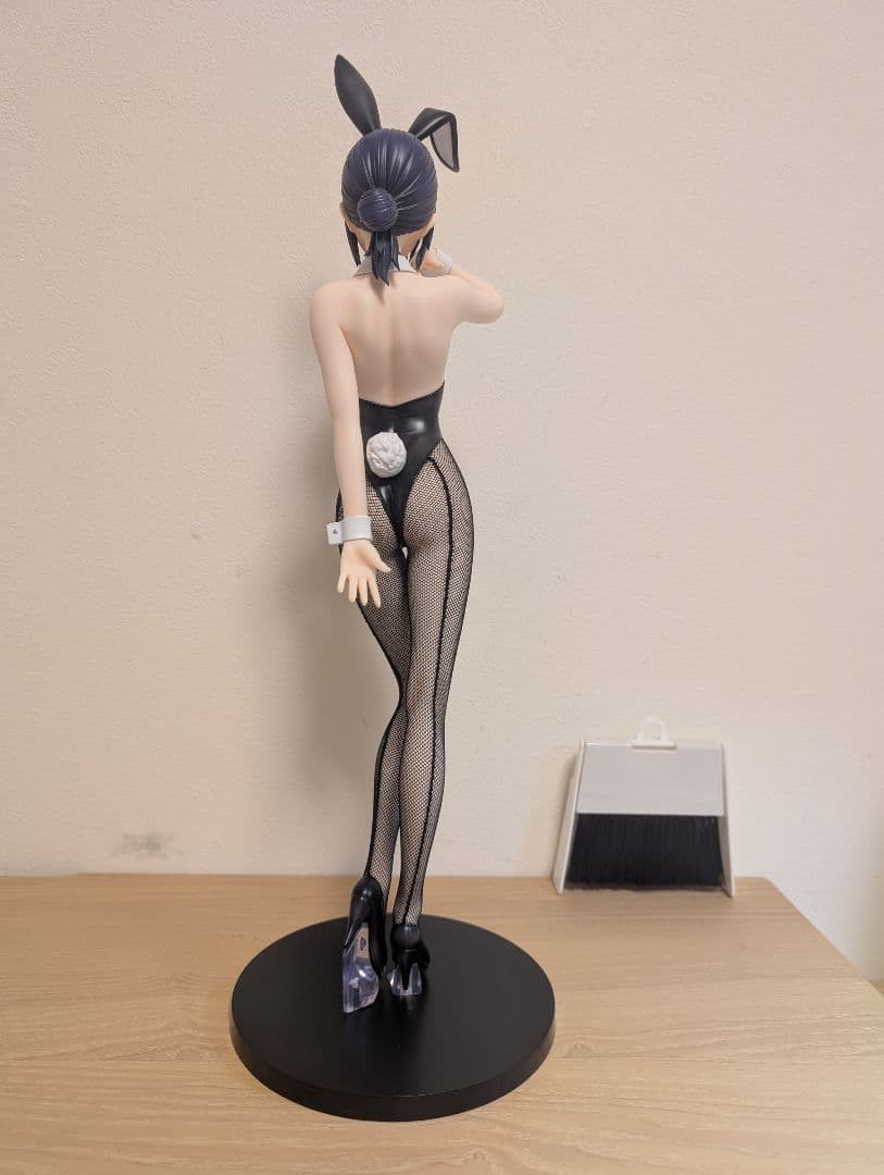 Rear view of a bunny figure with dark hair, black outfit and fishnet tights on a round black base.