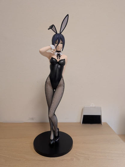 Blue-haired bunny figure in a black outfit and fishnet tights on a round black base atop a wooden table.