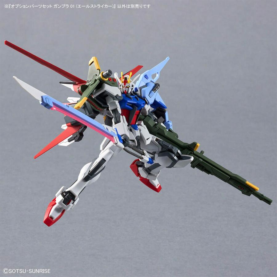 A Gundam model in a dynamic flying pose with a large green rifle and red and blue wings.
