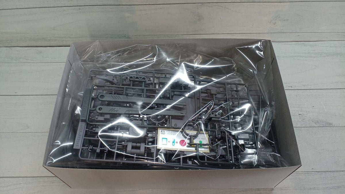 Gray model kit runners and a sticker sheet sealed in clear plastic inside an open box.