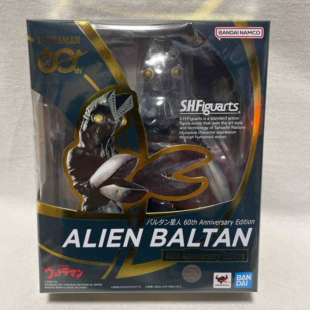 Front of a boxed S.H.Figuarts Alien Baltan 60th Anniversary Edition figure on a textured fabric surface.