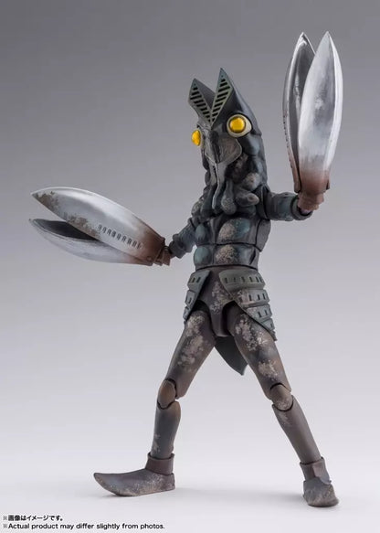 Alien Baltan figure with yellow eyes and large silver claws posed with arms raised on a gray background.