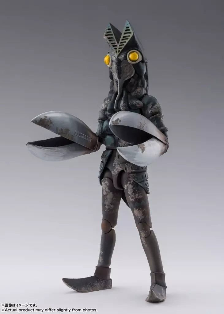 Alien Baltan figure with yellow eyes, large open silver claws and weathered detailing on a gray background.