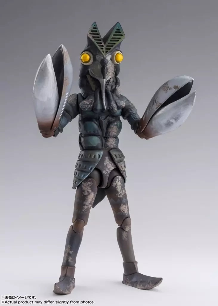 Alien Baltan figure with yellow eyes and raised silver claws against a plain gray studio background.