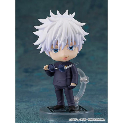 White-haired Gojo figure in a dark school uniform holding sunglasses, on a clear stand against a teal backdrop