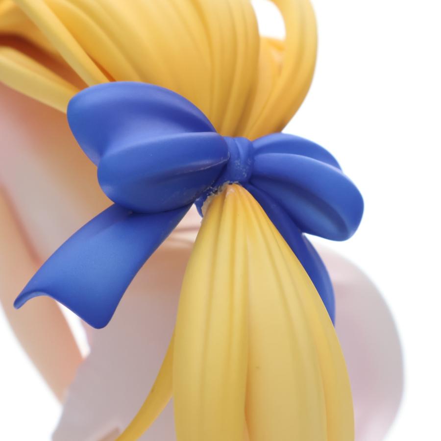 Close-up of a blonde figure's hair tied with a large blue ribbon on a white background.