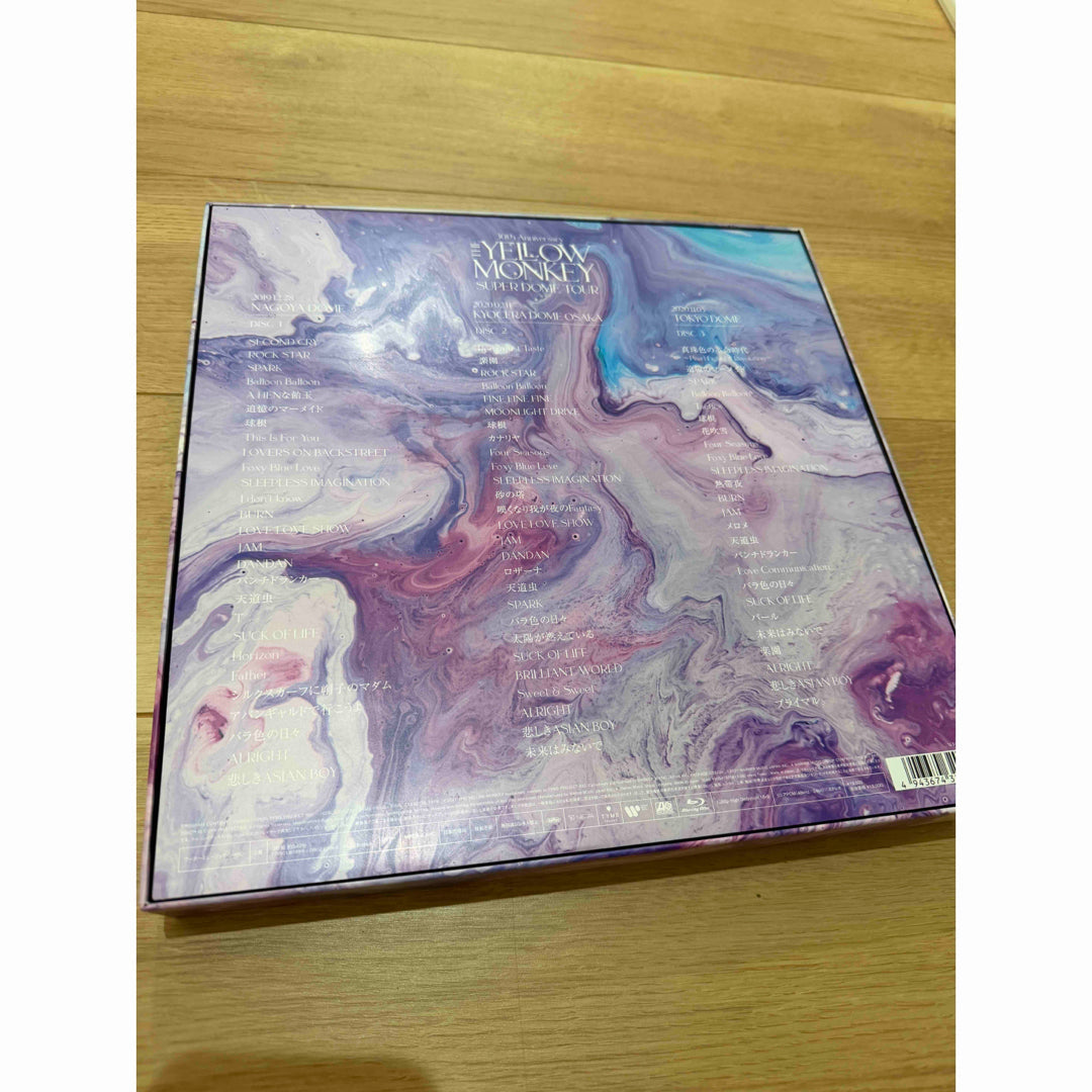Back of THE YELLOW MONKEY SUPER DOME TOUR box with marbled artwork and track lists on a wooden floor.